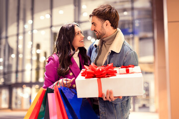 couple with bags and gift box enjoying winter shopping outdoors