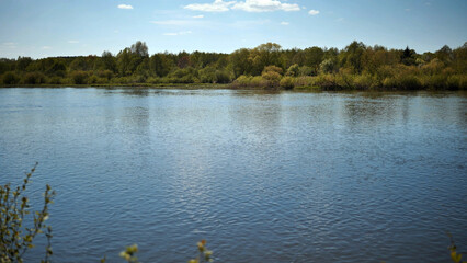 Reflection in the Neman River of cumulus clouds and the river bank overgrown with bushes and trees. Belarus region.