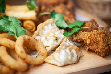 Gyoza dumplings background. Deep fried cripsy food. Fried chicken wings. Onion rings on wooden plate. Plate of deep fried food. Patry dish of food snacks. Family sharing plate of food.