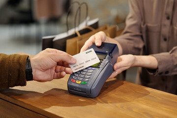 Hand of unrecognizable male consumer holding credit card over terminal screen during contactless...