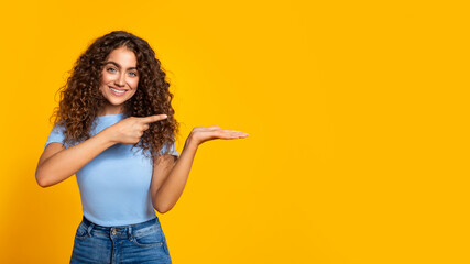 Cheerful woman presenting with hand on yellow, free space