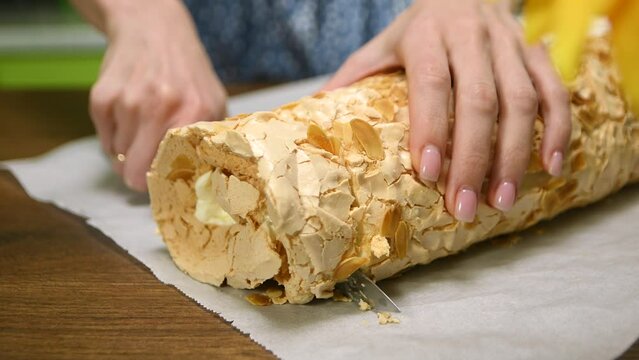 Woman cutting dessert meringue roll with cream in the kitchen, close up
