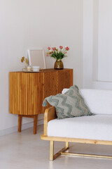 Naklejka premium Modern living room featuring a white couch, wooden sideboard, and a vase of flowers. A white curtain with small lights forms the backdrop. Concept: Cozy home interior. Copy space available.
