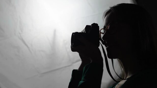 Sillhouete of cheerful female photographer capturing pictures with a dslr camera. Creative young woman smiling happily while using a camera in her home studio.
