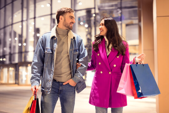 Millennial couple enjoying winter shopping trip carries bags outside mall