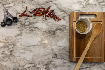 Dark wood cutting board on marble background with copy space. Chili peppers, oregano and wooden spoon on right