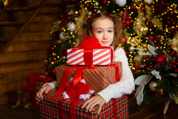 A happy girl holds a lot of boxes with Christmas gifts, unpacks a package with New Year's gifts, unpacks the received package, smiles at the camera, smiles. Christmas portrait.