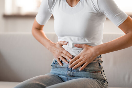 Unrecognizable young woman touching aching stomach feeling abdominal pain indoor