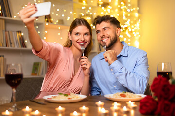 Couple taking a selfie with wine at a candlelit dinner, joyful