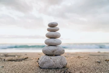 Fotobehang A cairn of smooth stones stacked on the sand symbolizes balance and tranquility by the sea © arthurhidden