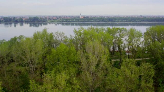 Drone flight above wooded area and river towards small town Beocin, Serbia