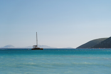 Obraz premium A lone sailboat drifts on the expansive blue waters under the vast sky, framed by distant hills