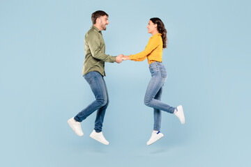 Joyful couple holding hands and jumping, blue background