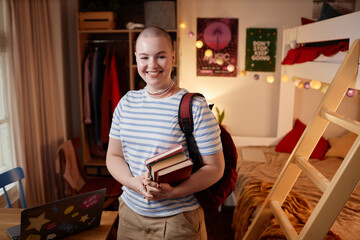 Waist up portrait of bald young woman as female student smiling at camera and holding books in...