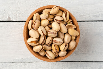 Overhead shot of roasted pistachios in bowl on white wooden table. Healthy snacks
