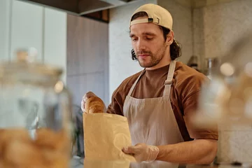 Gordijnen Caucasian male worker carefully packing takeaway order at bakery © AnnaStills