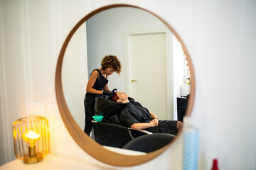 Hairstylist washing client's hair in a salon mirror reflection