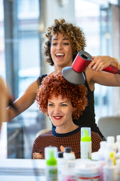 Stylist blow drying a client's curly hair at the salon
