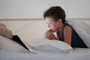 Little boy watching video on tablet while lying in bedroom