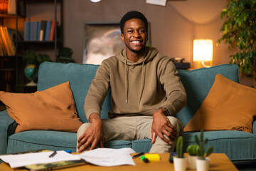 Photo of delighted dark skinned african american black man guy student sitting in the living room smiling having mess at home studying educational proess online from distance preparing for exams. - Powered by Adobe