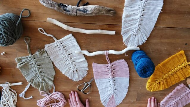 Top down view of woman making boho macrame feathers. Knitting macrame wall decor DIY. Flat lay of woman hands with macrame leaf or feather
