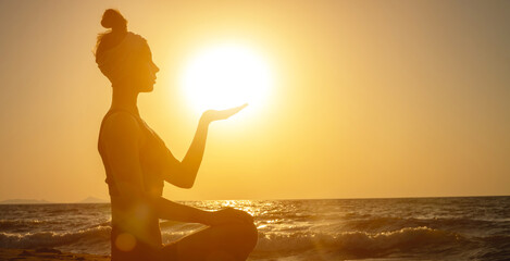 Side view of backlight and silhouette of young woman holding sun on the beach at sunrise or sunset. Spiritual practices in nature