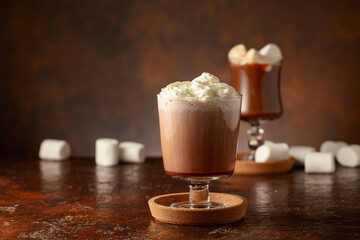 Hot chocolate with whipped cream in a glass mug on a old brown table.