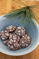 Delicious Crinkles, brown white chocolate flavored cocoa crinkle cookies covered with powdered sugar in blue bowl pine branch