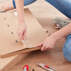 A woman sitting on the floor and opening a cardboard box with self-assembly furniture.
