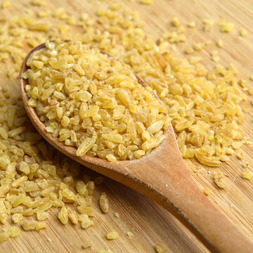 Cracked wheat daliya grains in wooden spoon, on bamboo cutting board