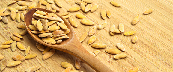 Roasted salted organic dry melon seeds, in wooden spoon on bamboo cutting board