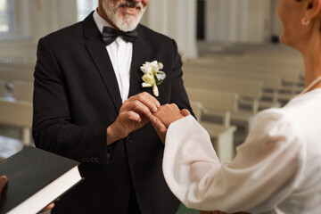 Closeup of senior groom exchanging rings with bride during wedding ceremony at church