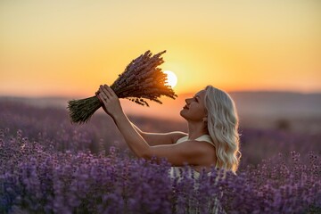 Blonde woman poses in lavender field at sunset. Happy woman in white dress holds lavender bouquet....