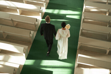 Top view at senior couple walking down aisle in church during wedding ceremony in sunlight, copy...