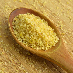 Cracked wheat daliya grains in wooden spoon, on bamboo cutting board