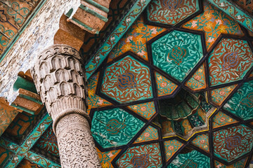 Wooden column support on the facade of a building supports the roof in the ancient city of Khiva in Khorezm, wood carvings and traditional patterns on the ceiling, interior - obrazy, fototapety, plakaty