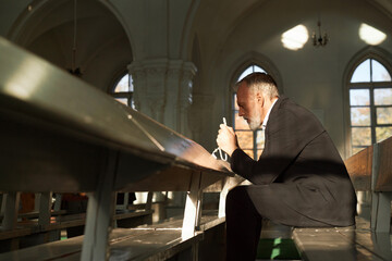 Side view portrait of senior man praying and holding rosary beads alone in church, copy space