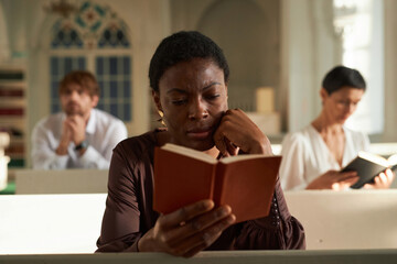 Portrait of adult African American woman reading Bible in church on Sunday