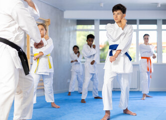 Determined boy in white kimono practicing punches in gym during martial arts workout with...