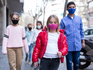 Focused preteen girl in pink protective mask walking along city street on spring day. New life...