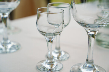 Empty wine glasses and shot glasses on a table with a white tablecloth.