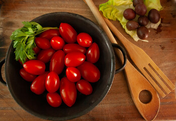Top photo of a rustic dish with small tomatoes and salad utensils.