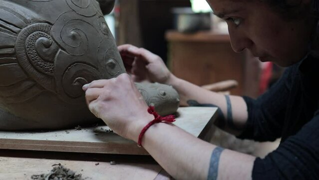 Close up of concentrated latin artist woman using sculpting caving tool to design an artistic clay pottery work.