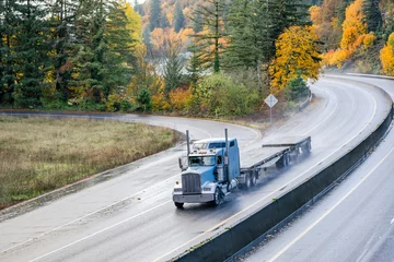 Foto op Canvas Light blue classic big rig bonnet semi truck tractor transporting two empty flat bed semi trailer driving on the wet autumn highway road with rain dust at rainy weather © vit