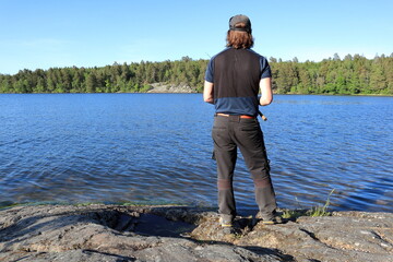 Fototapeta na wymiar Man fishing at some cliffs. Sunny summer day. Mälaren lake, Stockholm, Sweden.