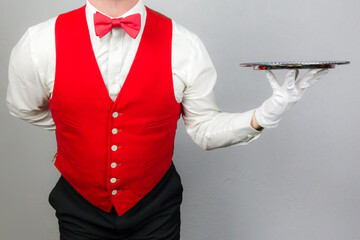 Portrait of Waiter in Red Vest or Waistcoat and Red Bow Tie Holding Silver Serving Tray. Concept of Service Industry and Professional Hospitality.