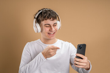 One man caucasian young male stand studio shot on beige background use mobile phone smartphone with headphones listen music send messages texting or browse internet online app copy space