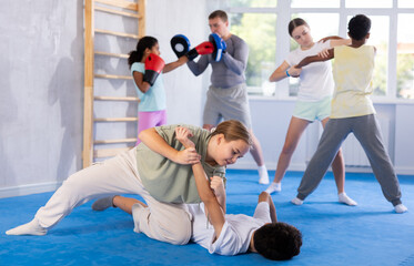 Focused teenage girl learning effective self defence techniques in sparring with boy, practicing...
