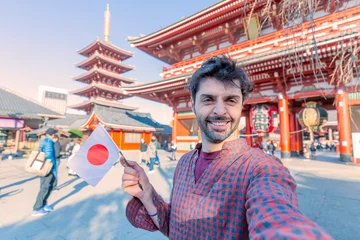 Zelfklevend Fotobehang Handsome young tourist enjoying summer holiday in Tokyo, Japan - Traveling life style concept with smiling man taking selfie on city street with japan flag- Tourism and summertime vacation concept © minoandriani