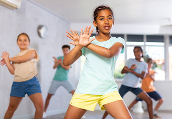 Dynamic little girl training Hip hop dance poses in dancehall with other attendees of dancing...